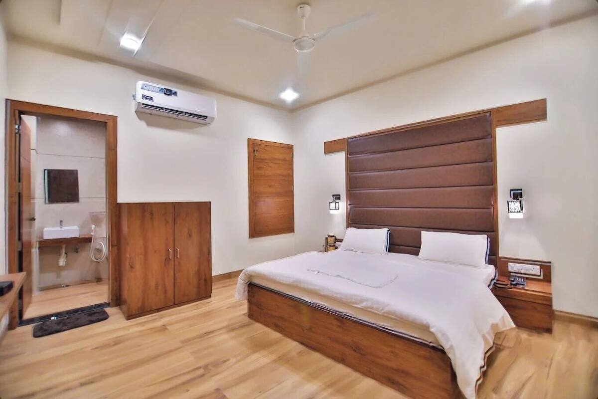 A bedroom with a wooden headboard, a bed with white linens, a ceiling fan, and an air conditioning unit.