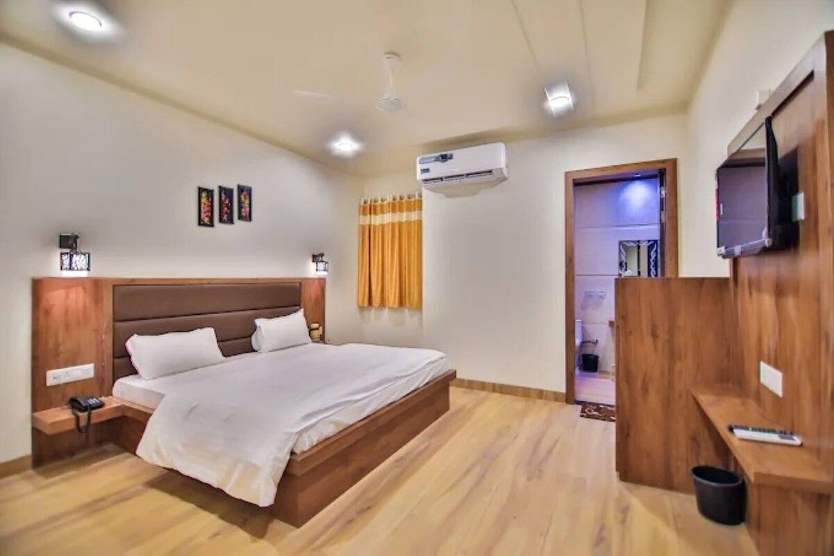 A bedroom with a wooden bed, bedside tables, an air conditioning unit, a television, and a small desk with a chair.