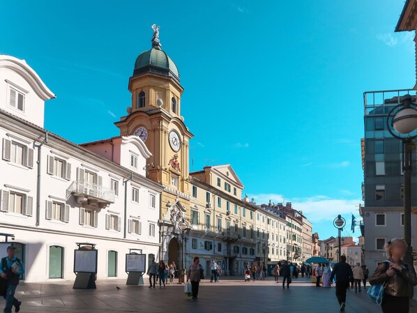 A spacious public square with historic buildings, a prominent clock tower, and a clear blue sky.