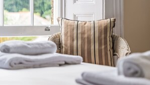 Una habitación con una silla de mimbre, un cojín a rayas y toallas dobladas con cuidado sobre una cama.