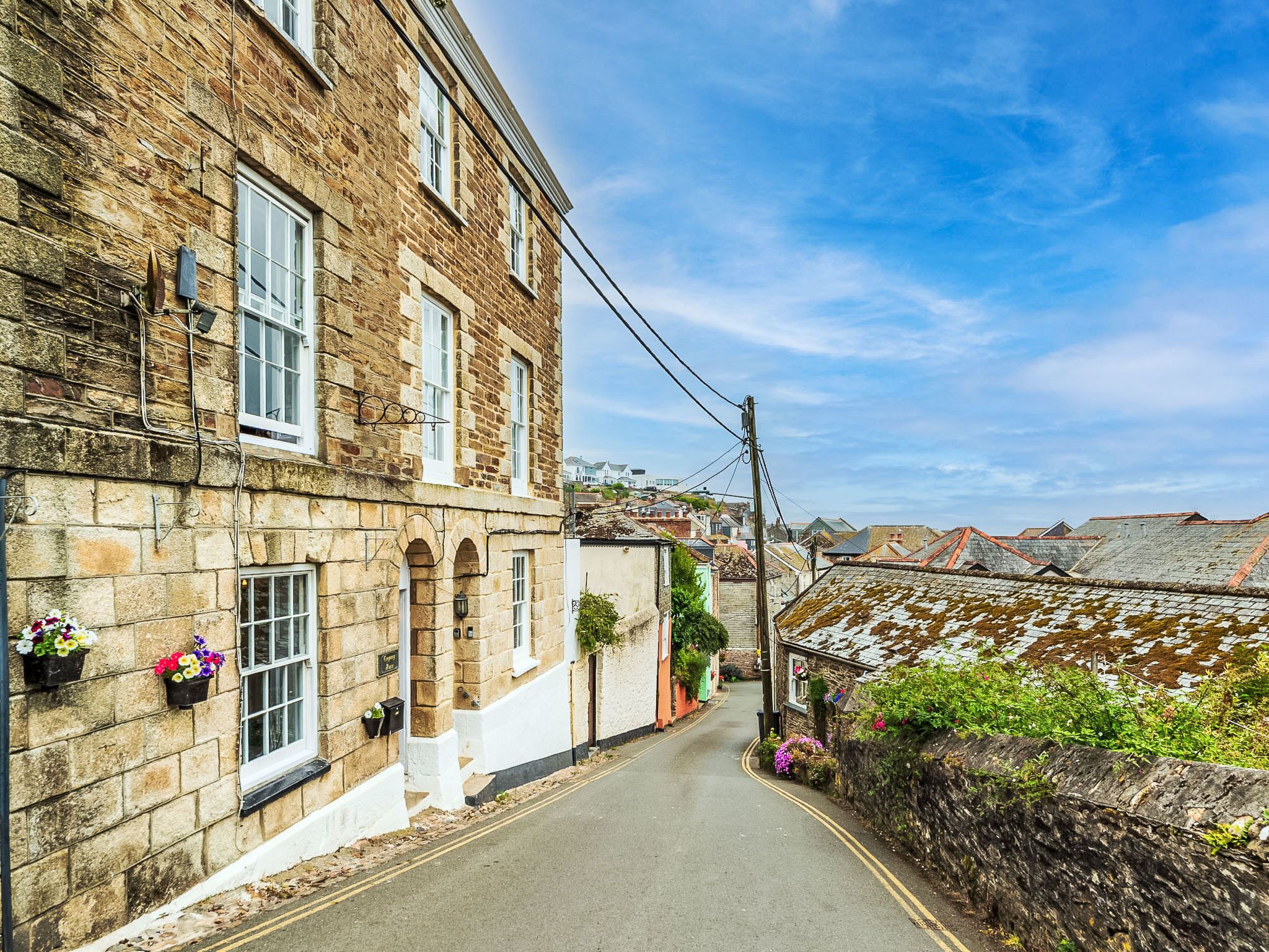 A narrow street with stone buildings, flower boxes, and a clear sky.
