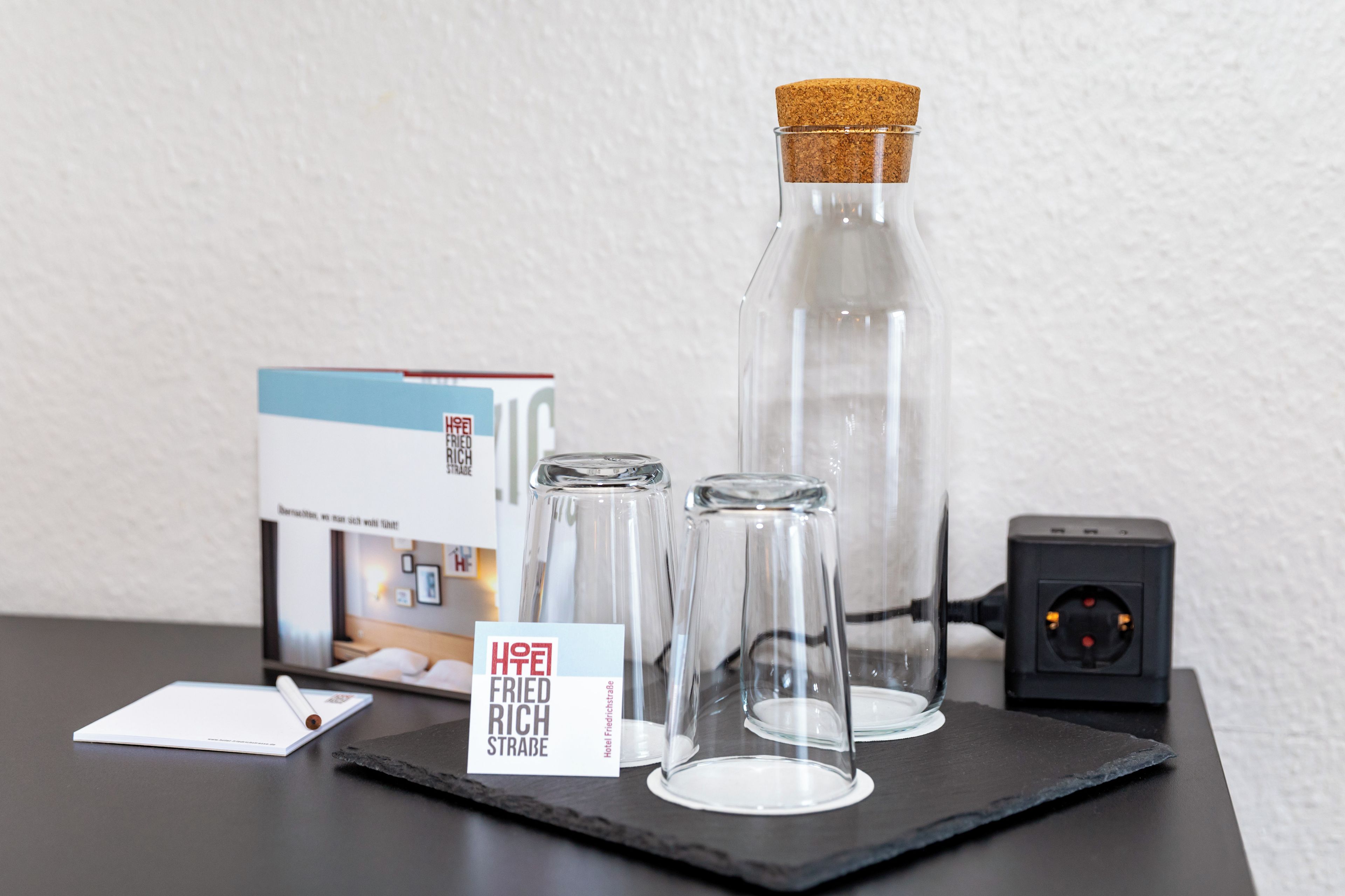 A table with a glass bottle, two glasses, a sign, a box, and a power strip.