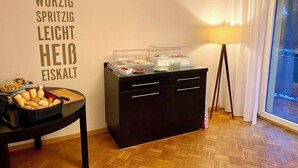 A room with a buffet setup, a wall with German words, a lamp, and a view through a window. - Hotel Friedrichstraße  (Lampertheim)