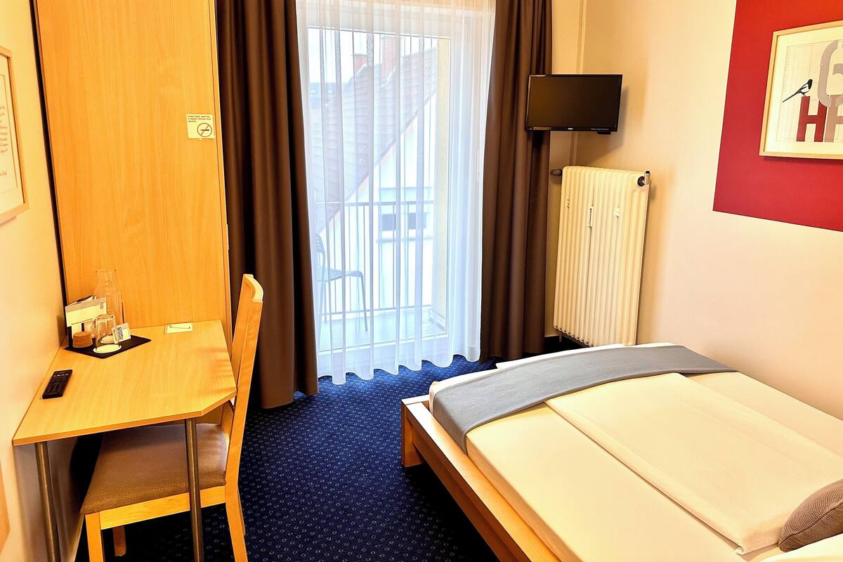 A hotel room with a bed, a desk, a chair, a TV, and a window with curtains.