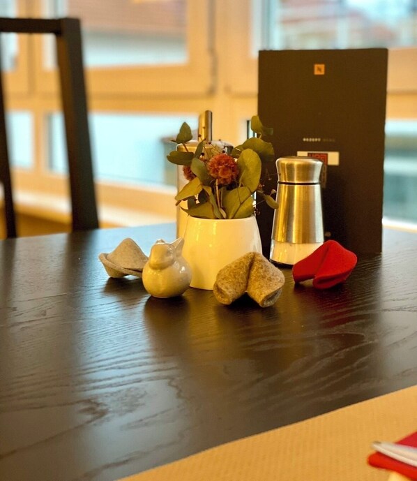 Ein Holztisch mit einer weißen Vase mit Blumen, einer silbernen Kaffeekanne und kleinen Dekorationen.