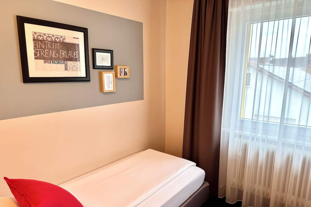A hotel room with a bed, a red pillow, and framed pictures on the wall.