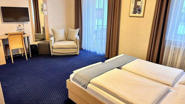 A hotel room with a bed, a desk, a chair, a TV, and a window with curtains. - Hotel Friedrichstraße  (Lampertheim)
