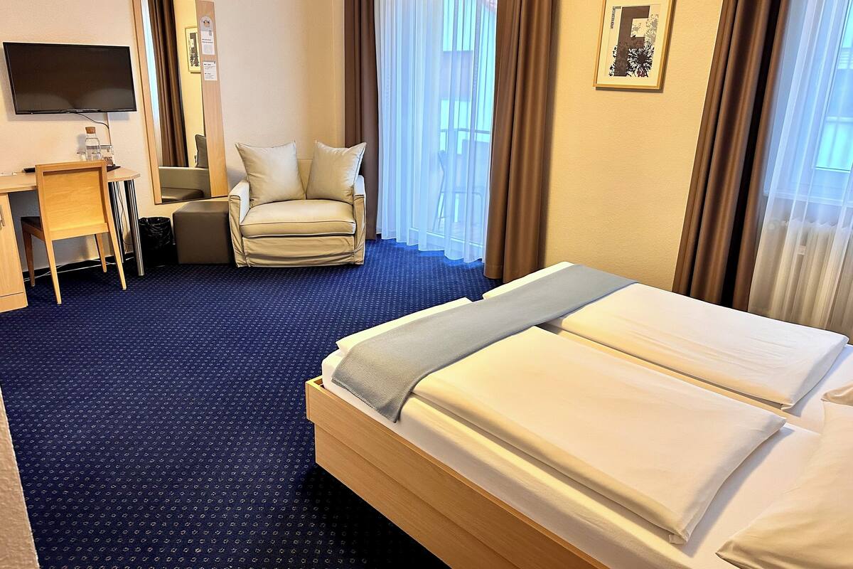 A hotel room with a bed, a desk, a chair, a TV, and a window with curtains.