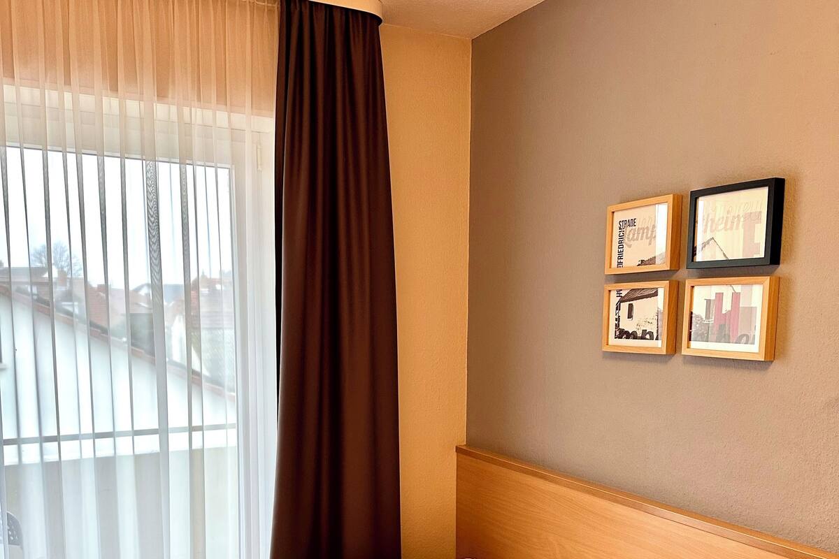 A hotel room with a bed, a window with sheer curtains, and framed pictures on the wall.