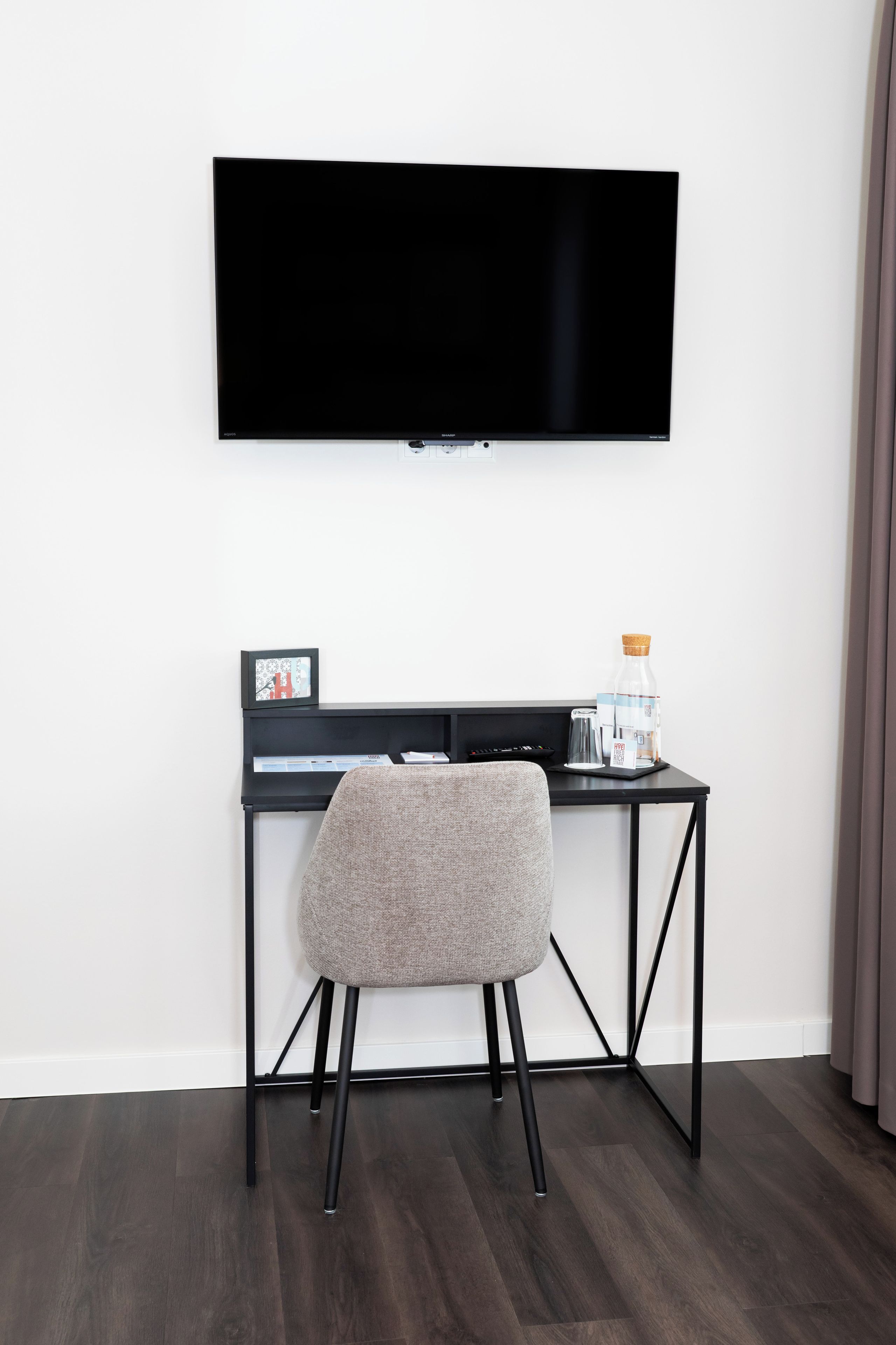 Ein modernes Wohnzimmer mit einem an der Wand befestigten Flachbildfernseher, einem schwarzen Schreibtisch mit Stuhl und einer Kaffeemaschine.