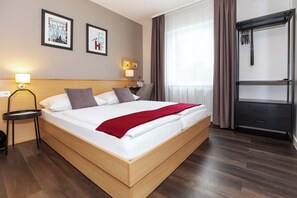 Habitación de hotel con una cama grande, una mesita de noche con lámpara, un armario y dos cuadros en la pared.
