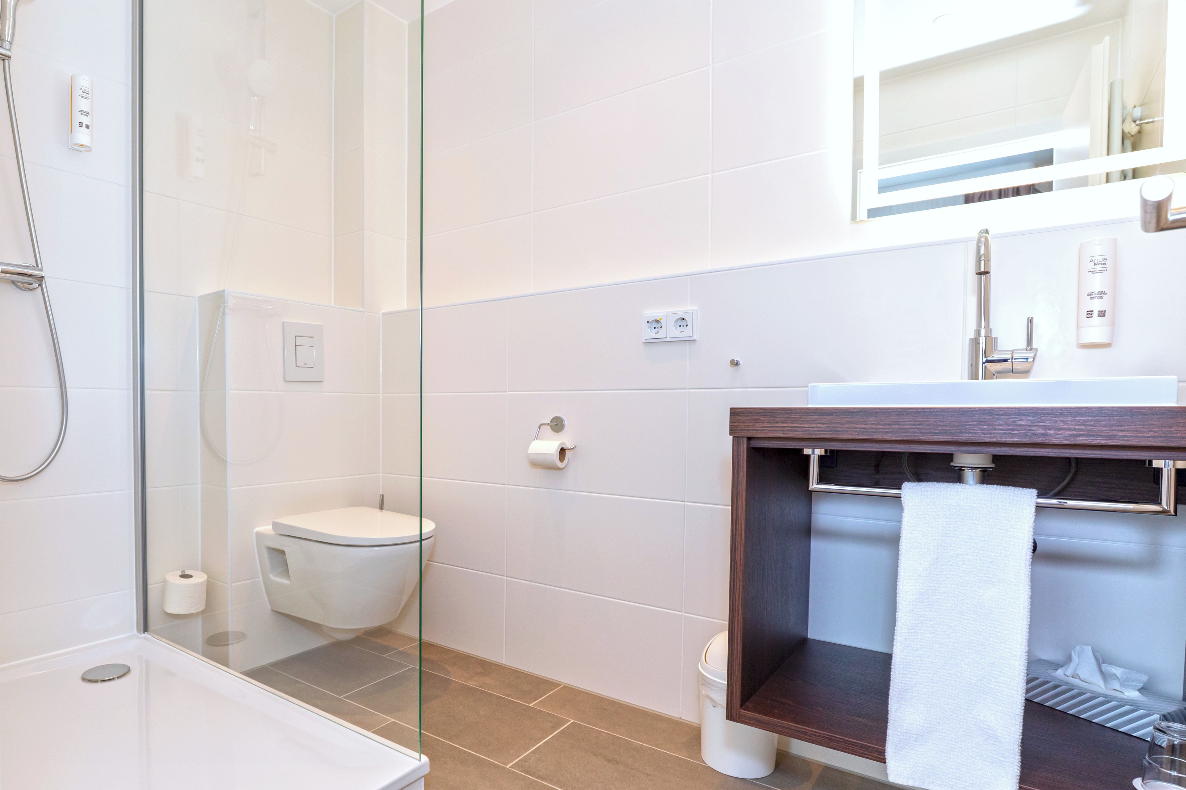 Ein modernes Badezimmer mit Duschkabine aus Glas, Toilette, Waschbecken mit Handtuchhalter und Spiegel über dem Waschbecken.