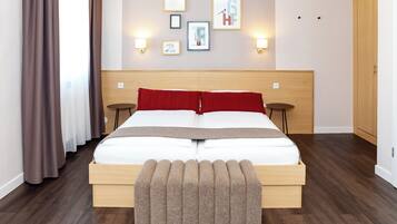 Habitación de hotel con cama de madera, dos mesitas de noche, un banco al pie de la cama y una pared con cuadros enmarcados y luces fijadas a la pared.
