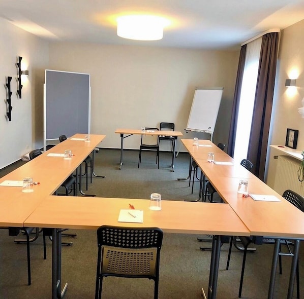 Un salón de conferencias con largas mesas, sillas, una pizarra y una pantalla de proyector.