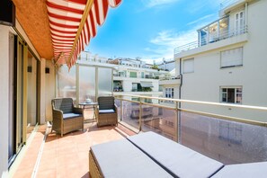 Un balcone con mobili in vimini, un tenda a righe e vista sugli edifici circostanti.