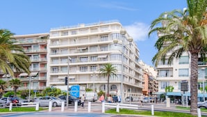 A multi-story hotel with balconies, a pedestrian walkway, and palm trees. - Apartment with Private Terrace, Wi-Fi and Air Conditioning (Nice)