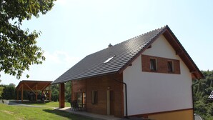 A two-story house with a sloped roof, a covered porch, and a small outdoor seating area. - Vacation home Dola II in Bohemian Paradise with pool (Mírová pod Kozákovem)