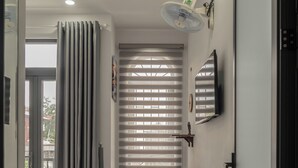 A modern bedroom with a bed, a standing fan, a TV, and a window with blinds. - Soul Station Studio Hotel II (Ho Chi Minh City)