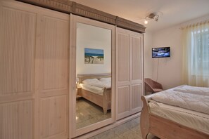 A bedroom with a bed, a TV, a wardrobe, and a painting on the wall.