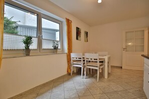 Une pièce comprenant une table et des chaises, une fenêtre avec des stores, une porte dotée de panneaux en verre dépoli et une plante en pot posée sur le rebord de la fenêtre.