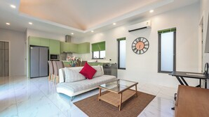 A modern living room with a sofa, coffee table, and a kitchen in the background. - 3BR PoolVilla 7 Mins to Nai Harn V108 (Rawai)