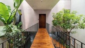 En korridor med trægulv, metalgelændere og store, grønne planter langs begge sider.