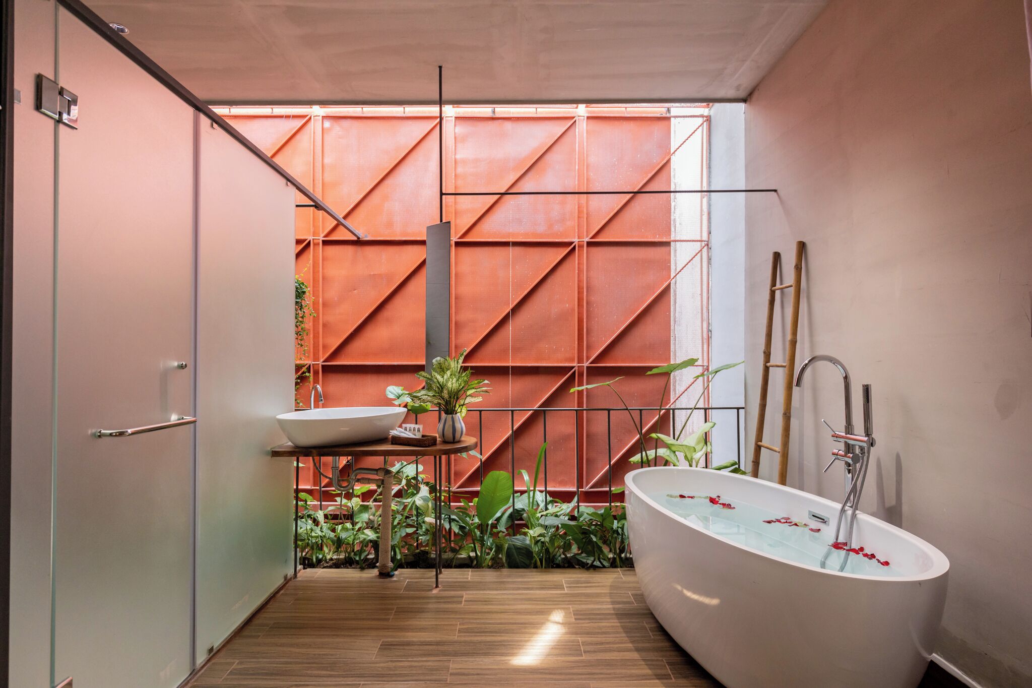 A modern bathroom with a freestanding bathtub, a sink, and a large window with a view of a red wall and plants.