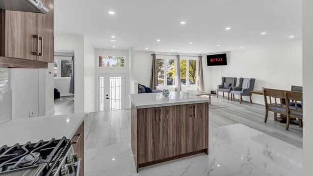 A modern kitchen with a central island, a dining area with wooden furniture, and a flat-screen TV mounted on the wall. - Spacious home with 6 Beds (Brampton)