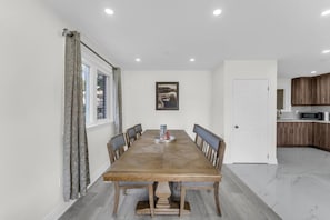 Uma sala de jantar com mesa e cadeiras de madeira, uma cozinha com armários de madeira e uma porta branca.