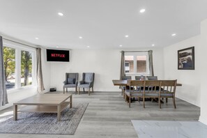 Ein modernes Wohnzimmer mit Fernseher, zwei Sesseln, einem Holzesstisch und einem Teppich.