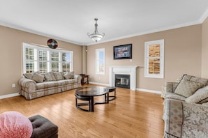 Een woonkamer met een open haard, twee banken, een salontafel en houten vloeren.