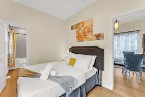 Une chambre à coucher comprenant un lit, une tête de lit, un tableau et un coin repas avec des chaises.