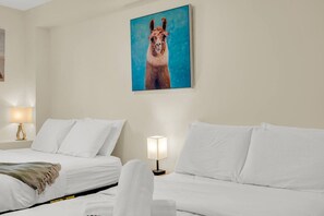 A hotel room with two beds, a painting of a llama, and a lamp on each side.