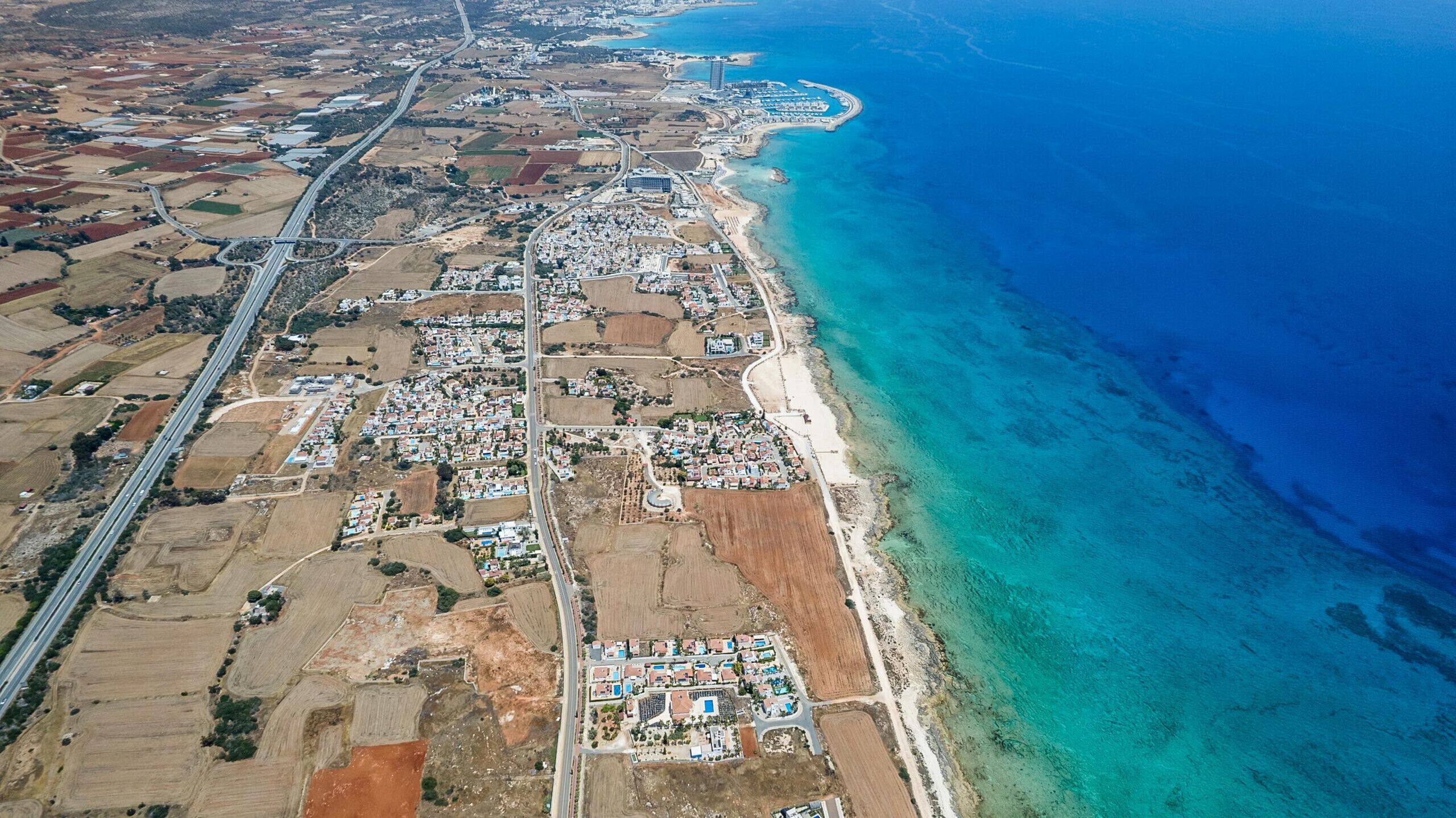 Vue aérienne d’une ville côtière avec une plage, des zones résidentielles et une autoroute principale.