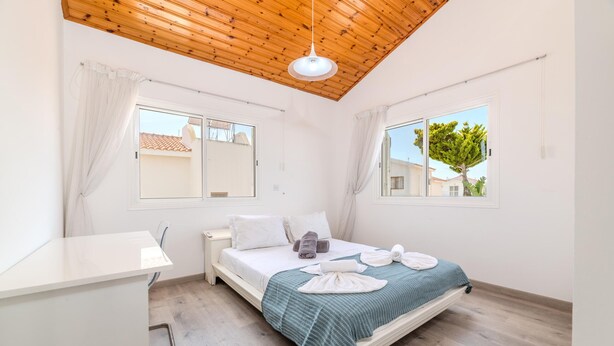 A bedroom with a wooden ceiling, a bed with a green blanket, a bedside table, and a window with curtains. - La Casa De Louie Villa (Sotira)