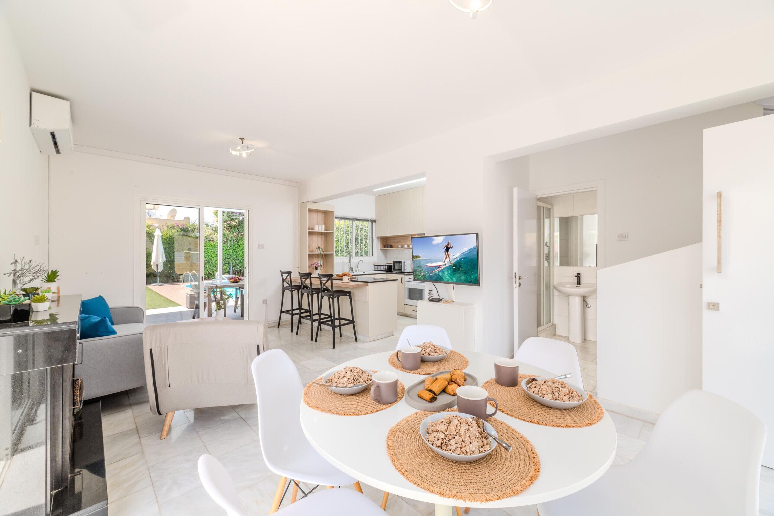 A modern kitchen with a dining area, large windows, and a TV.