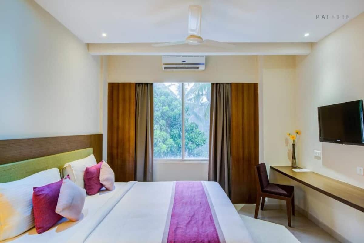 A hotel room with a bed, a desk, a chair, a TV, and a window with curtains.