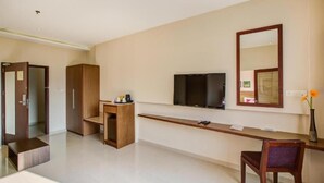 Et moderne hotelværelse med et fladskærms-tv på væggen, et træskrivebord, en stol og et garderobeskab.