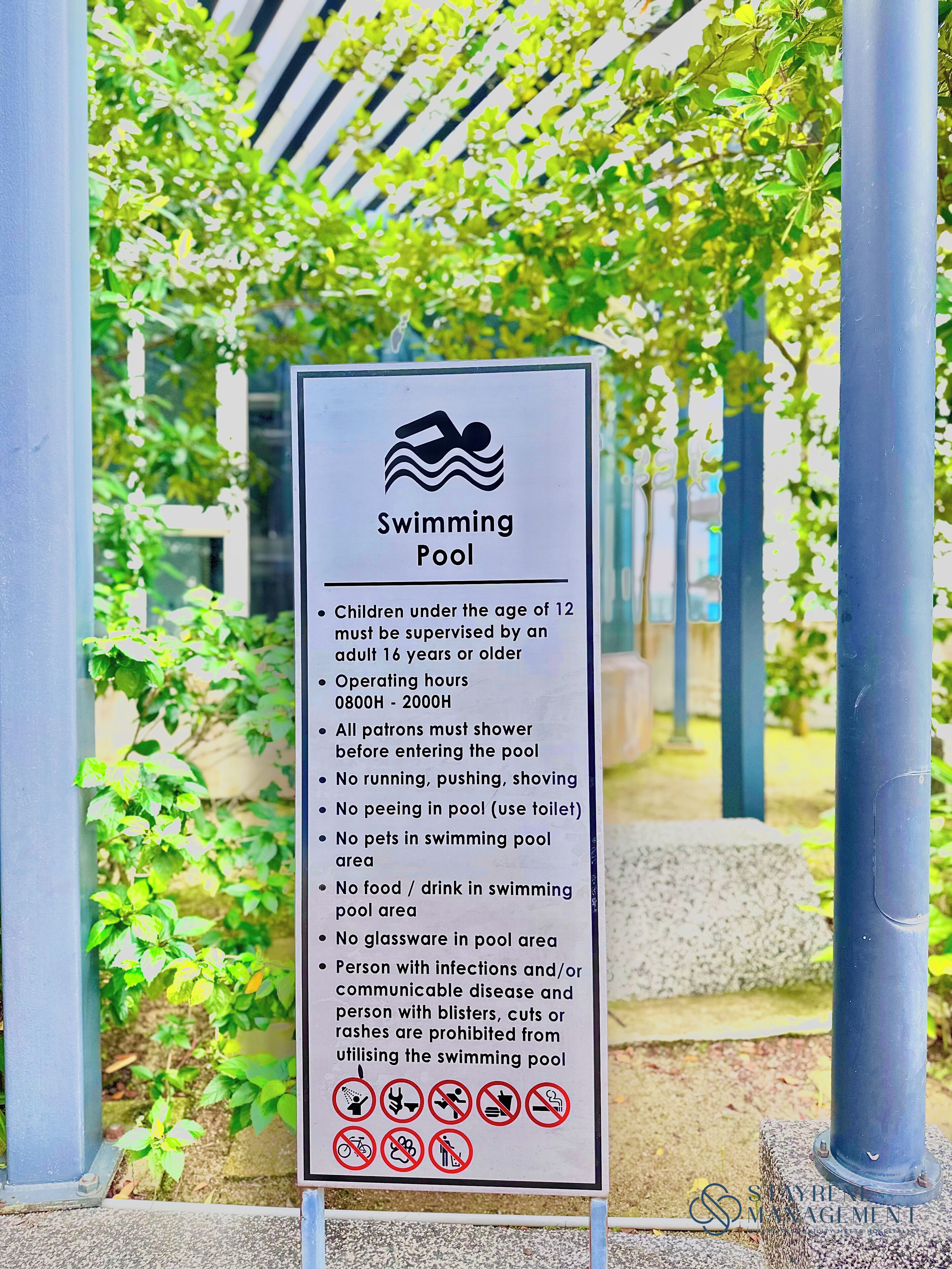 A sign detailing rules for a swimming pool area, including operating hours and restrictions on activities and personal items.