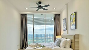Un dormitorio moderno con una cama grande, un ventilador de techo y vistas de la ciudad a través de ventanales.