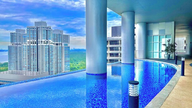 Un hotel moderno con piscina infinita en la azotea, grandes pilares y vistas a edificios altos.