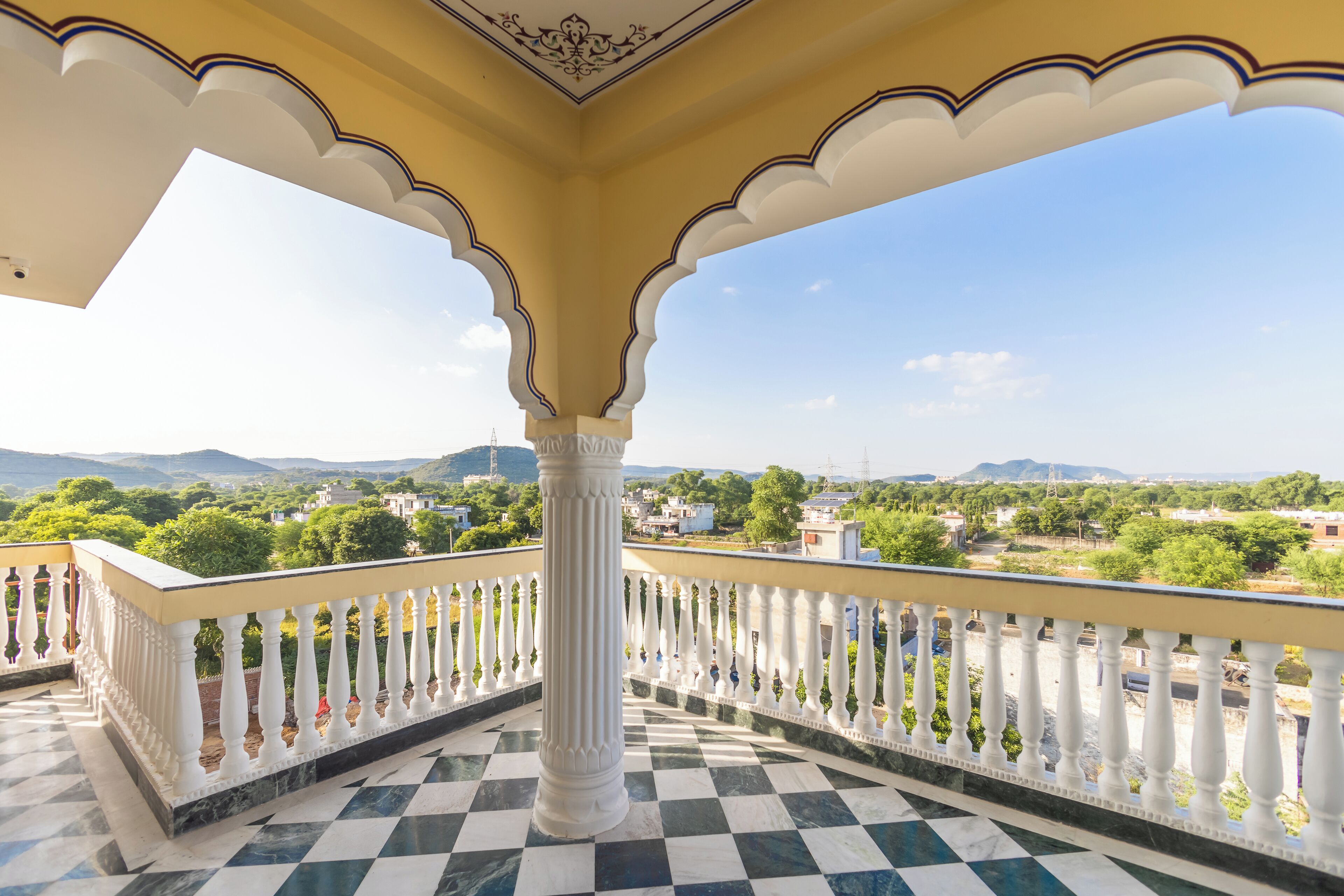 Un balcón con piso a cuadros, barandillas blancas y vistas a un paisaje lejano.
