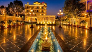 Un patio de hotel con una fuente central, un edificio amplio con varios balcones y un paseo bien iluminado.