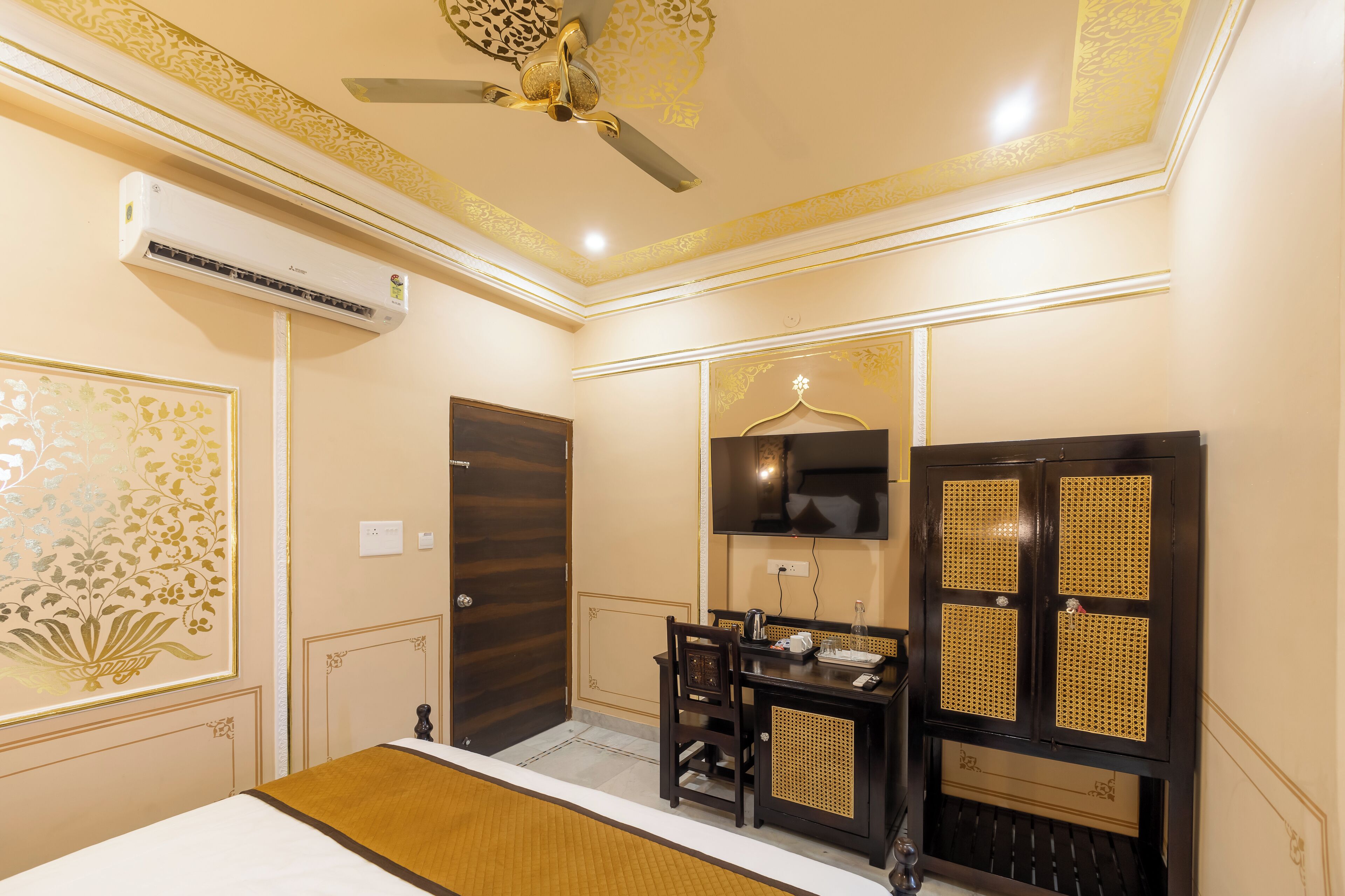 A hotel room with a bed, a desk with a chair, a television, and an air conditioning unit.