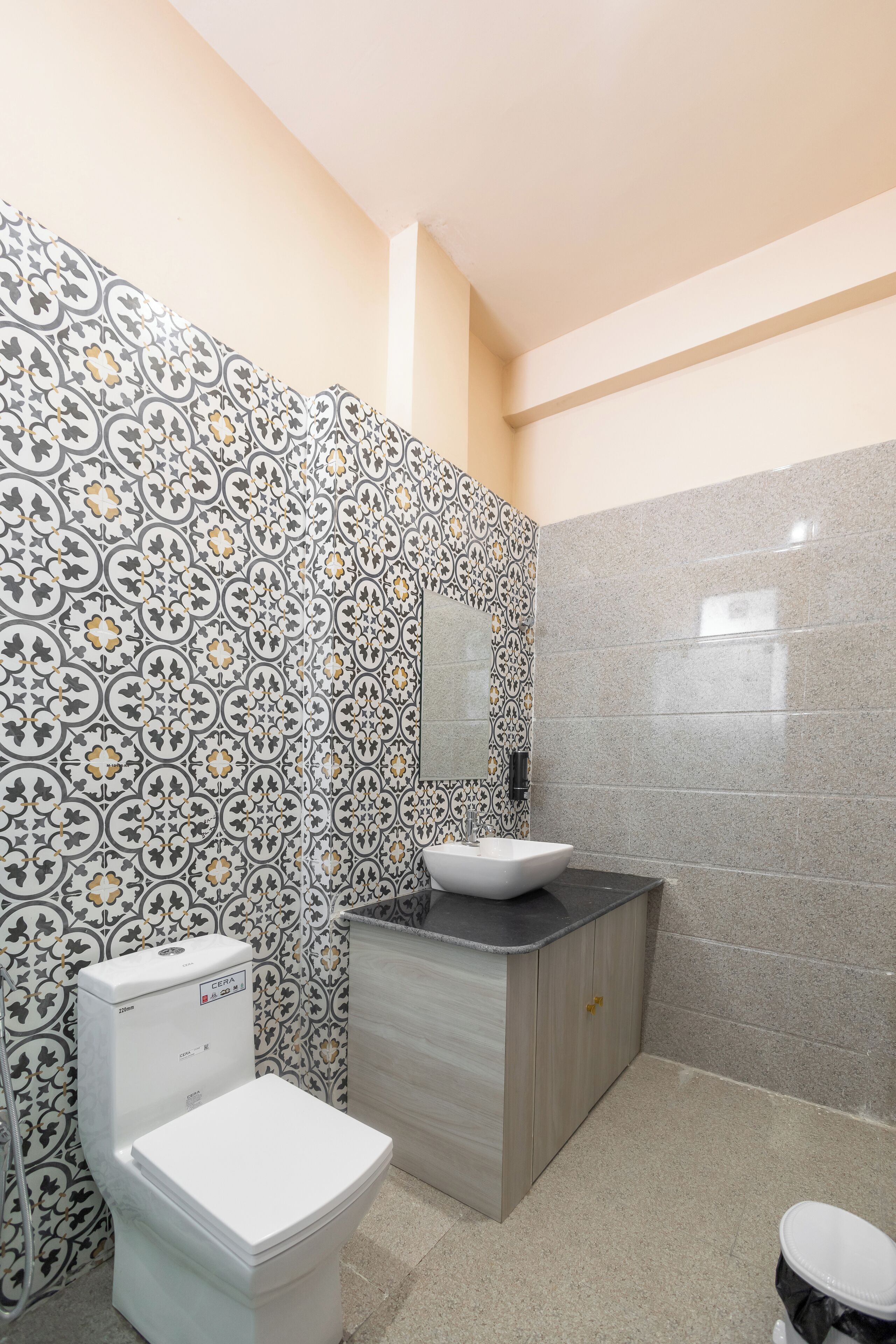 Ein Badezimmer mit Wandfliesen mit Muster, einer weißen Toilette, einem Waschbecken mit Spiegel und einem Schrank.
