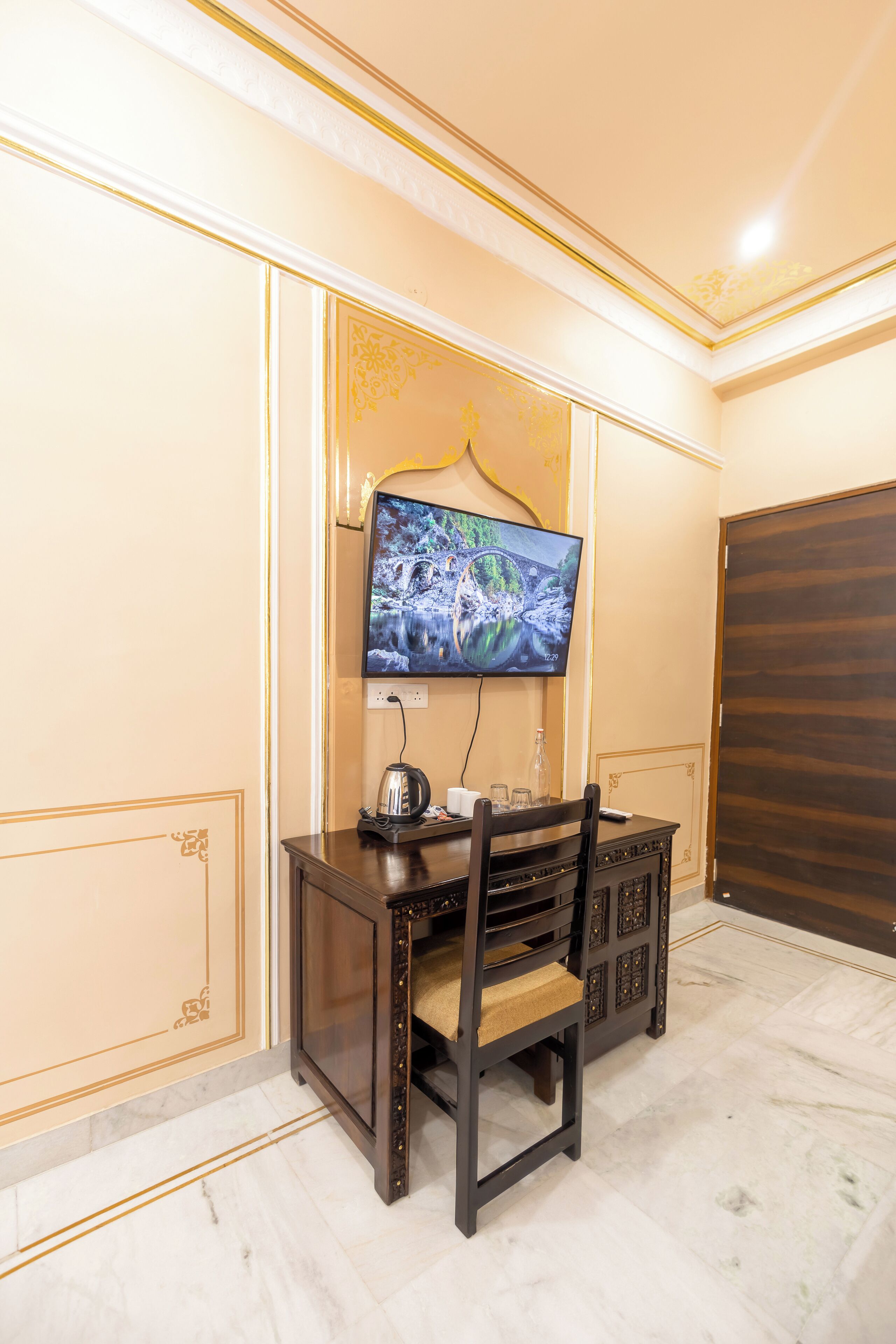 Ein Zimmer mit an der Wand montiertem Fernseher, einem Holztisch mit Stühlen und einem Marmorboden.