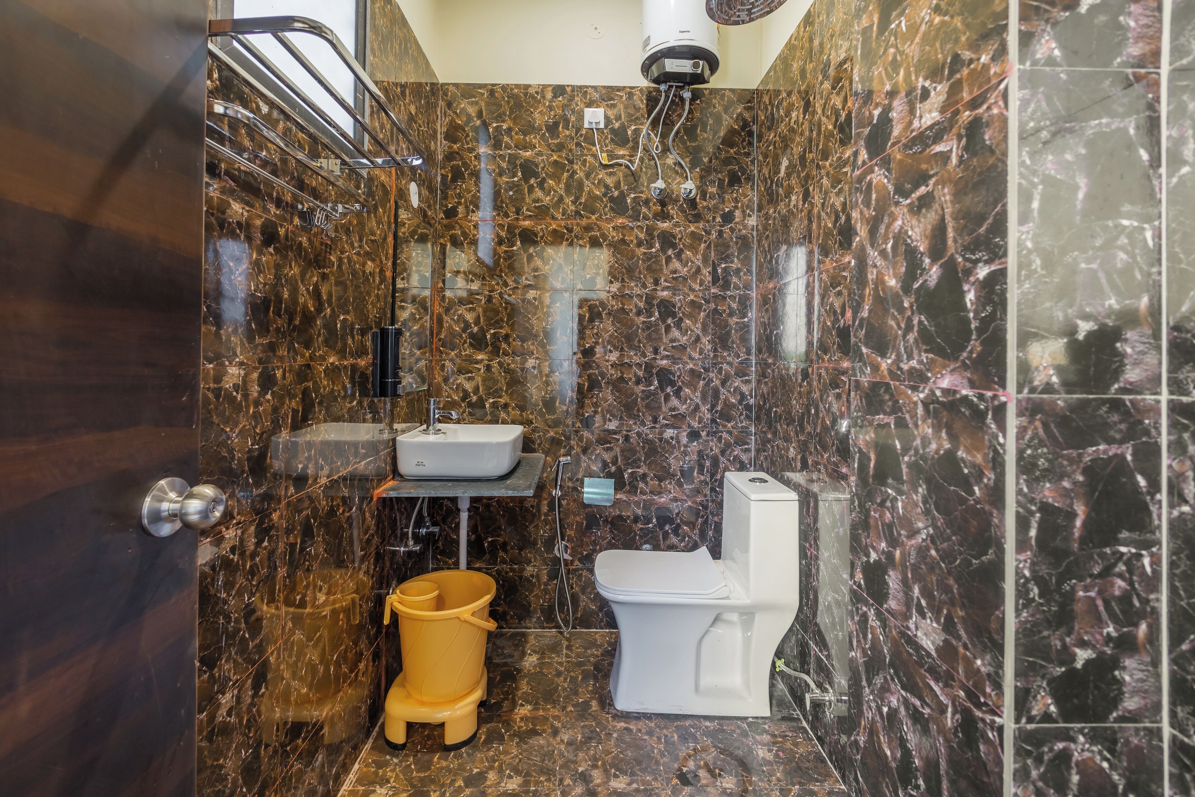 Un baño con pared de mármol, inodoro blanco, lavabo y un cubo amarillo.