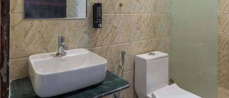 A bathroom with a marble wall, a sink, a toilet, and a shower enclosure.