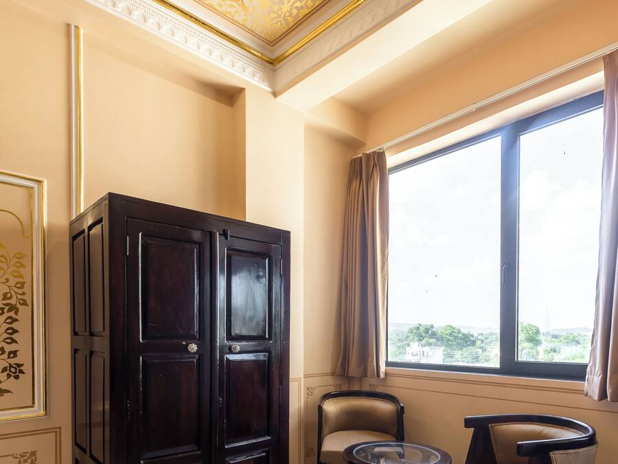 A room with a dark wooden cabinet, two chairs, a small round table, and a large window with curtains.