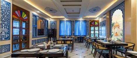 A restaurant with multiple tables and chairs, blue and white patterned walls, and a tiled floor.